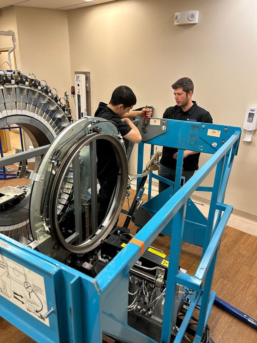 Two technicians dismantling a CT gantry supported on a blue rigging frame